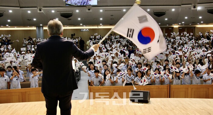 새로남교회 오정호 목사가 위문 행사에 참석한 참전용사 및 성도들, 새로남기독초등학교 학생들과 태극기를 흔들며 '우리의 소원은 통일'을 합창하고 있다. 