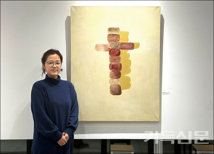 황은아 작가가 ‘돌 십자가’를 주제로 한 자신의 작품 앞에서 미소 짓고 있다.