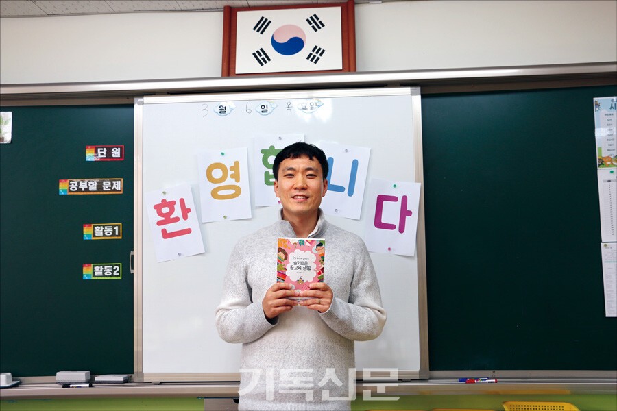 공교육 제도 안에서 믿음의 자녀를 양육하기 원하는 학부모들을 위해 책을 쓴 현직 교사 김병화 선생을 새 학년 새 학기 첫날 만났다. 그가 담임하는 교실에서 자신의 책 [슬기로운 공교육 생활]을 든 채 웃어 보이고 있다.